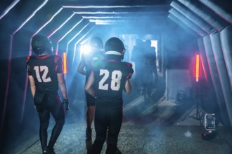 American football players wearing jerseys and helmets, emerging from a dark tunnel towards a bright
