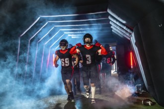 American football players in black and red uniforms and helmets running through a dramatic, smoke