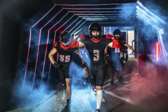 American football players are running forward from a dark stadium tunnel filled with blue and red