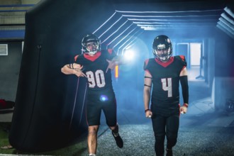 American football players in black and red uniforms and helmets are making an entrance, emerging