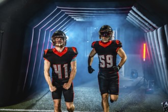 American football players in uniforms and helmets are stepping out from a dimly lit tunnel onto a