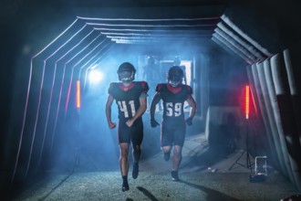 American football players burst from a smoky stadium tunnel in helmets and jerseys, running onto