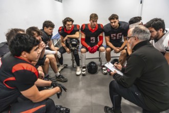 American football coach explaining game strategy to his young diverse football team members, who