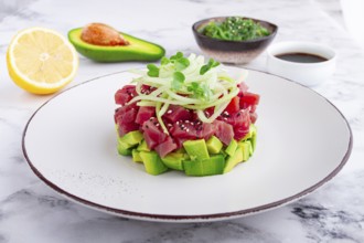 Fresh tuna tartare with avocado served on a marble table with soy sauce and seaweed salad