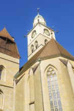 Gothic church tower with striking clock and pointed roofs in front of a bright blue sky, St