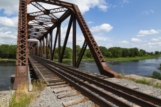 Railroad tracks leading to old rusted Terrebonne Pratt truss railroad bridge over Des Mille-Iles