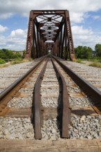 Railroad tracks leading to old rusted Terrebonne Pratt truss railroad bridge over Des Mille-Iles