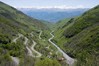 A green wooded valley with winding roads snakes through the mountains in the distance, serpentine
