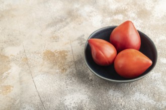 Red Heart shape tomatoes in blue bowl on brown concrete background. Side view, copy space. healthy