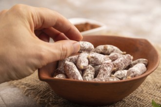 Small smoked Chicken sausages in clay bowl with hand on brown concrete background and linen textile