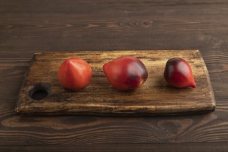 Red Heart shape tomatoes on cutting board on brown wooden background. Side view, copy space.