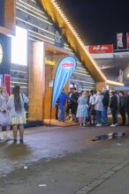 People standing in front of an illuminated marquee at night while waiting for admission,