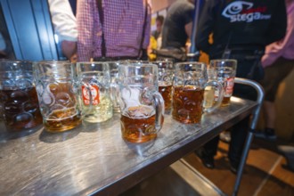 Row of beer mugs on a long wooden table at a festive event with people in the background,