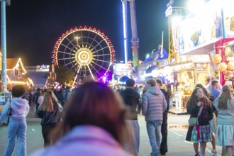 View of a busy fairground at night with an illuminated Ferris wheel and people waiting to go for a