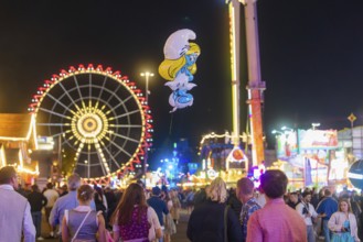 People enjoying the hustle and bustle of a fairground at night with a large Ferris wheel in the
