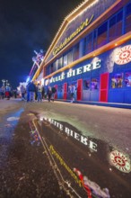 Reflection of the colourful lights of a beer hall on a wet street at night, Cannstatter Wasen folk
