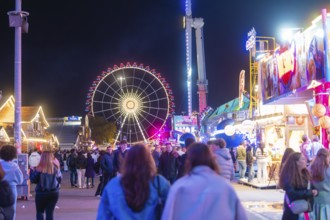 Lively funfair at night with lots of people and a large, illuminated Ferris wheel, Cannstatter