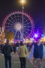 Large Ferris wheel at night, surrounded by a lively crowd, Cannstatter Wasen folk festival,