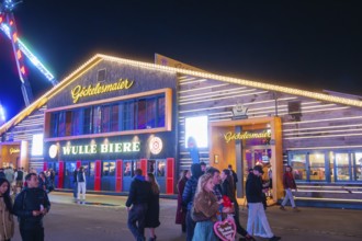 Illuminated building at night at the funfair with people passing by, Cannstatter Wasen funfair,