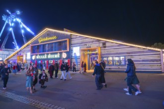 Visitors walk past an illuminated building at the funfair at night, Cannstatter Wasen funfair,