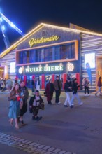 People strolling at night in front of an illuminated building at the funfair, Cannstatter Wasen