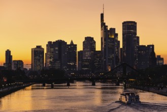 As a ship travels along the Main, the evening sky behind the Frankfurt banking skyline glows orange
