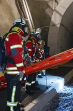 Firefighters in protective clothing stand ready at the tunnel entrance at night, firefighting