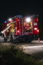 Fire engine at night with open back, illuminated by lanterns and blue lights, fire brigade exercise