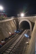 Rescue workers working in an illuminated tunnel at night, railway tracks in the foreground, fire