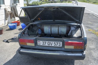 Old car with open boot, gas bottle and tools on a sunny day next to the road, car has gas tank