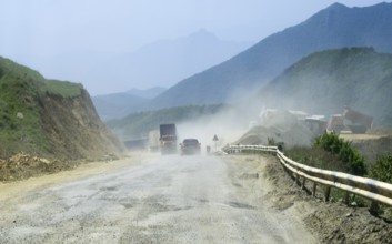 Dusty road with construction site in mountainous landscape with construction vehicles and lorries,