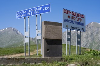 Signs on a roadside indicating the border to a place in a mountainous region, at the highest pass