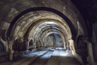 Interior view of an ancient vault with stone arches and a beam of light creating a mysterious