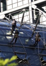 Three male glass cleaners abseiling down a glass roof of Berlin Central Station to clean windows,