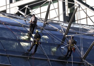 Three male glass cleaners abseiling down a glass roof of Berlin Central Station to clean windows,