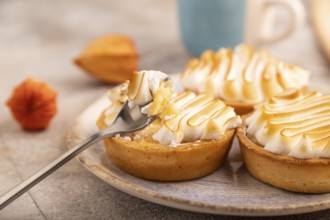 French lemon tart with meringue on brown concrete background, cup of coffee, orange linen textile,