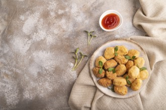 Fried crispy Chicken Nuggets with ketchup, microgreen on brown concrete background and linen