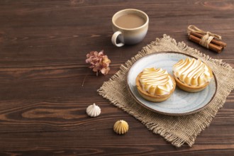 French lemon tart with meringue on brown wooden background, cup of coffee, linen textile, side