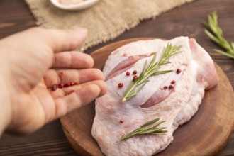 Raw Turkey Thigh with spices and rosemary on cutting board with hand on brown wooden background and