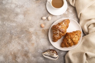 Croissant on white plate on brown concrete background and linen textile, cup of coffee, top view,