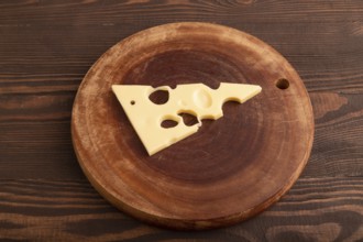 Piece of cheese with holes on cutting board on brown wooden background, side view, close up,