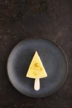 Yellow Cake pop with sprinkles on blue ceramic plate on black concrete background, top view, flat