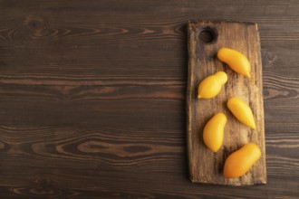 Yellow tomatoes on cutting board on brown wooden background. Top view, copy space, flat lay.