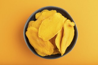 Dried Mango in blue ceramic bowl on orange pastel paper background. Top view, copy space, flat lay.