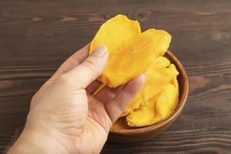Dried Mango in wooden bowl with hand on brown wooden background. Side view, close up. healthy food,