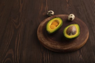 Two Avocado halves with pit and Egg yolk on round wooden cutting board on brown wooden background,
