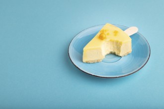 Bitten Yellow Cake pop with sprinkles on blue ceramic plate on blue pastel paper background, side