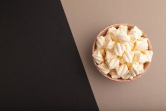 Orange and pink marshmallow in ceramic bowl on black and beige pastel paper background, top view,