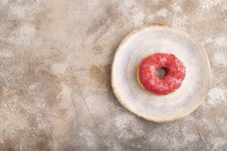 Pink Donut with sprinkles on blue ceramic plate on brown concrete background, top view, flat lay,