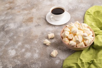 Orange and pink marshmallow in ceramic bowl on brown concrete background and green textile, side